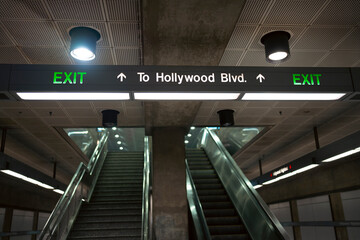 The sign shows directions for people using the subway. It points to an exit leading to Hollywood Blvd. The stairs are visible in the background, with lighting above.
