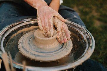 Fototapeta premium Clay pot forming on pottery wheel. Pottery shaping defines thickness, height, and symmetry before trimming and firing. Clay pot is shaped on the wheel to create stable ceramic form.