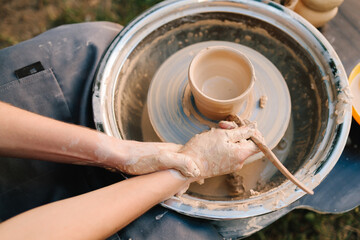 Fototapeta premium Clay pot forming on pottery wheel. Pottery shaping defines thickness, height, and symmetry before trimming and firing. Clay pot is shaped on the wheel to create stable ceramic form.