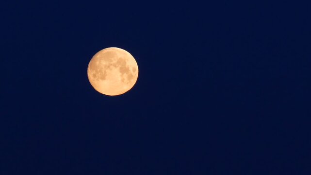 Full moon setting in the dark blue night sky
