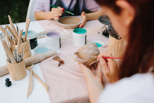 Ceramic painting of mug with fish pattern using brush strokes. Artist paints delicate purple fish on a handmade clay mug. Painting ceramic mug with purple fish using brush and paint.