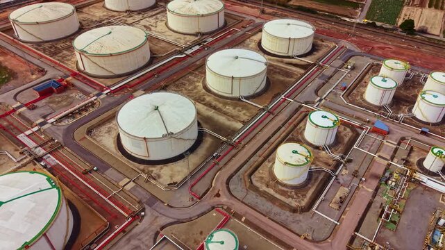 A view of multiple large storage tanks used for crude oil or petroleum products arranged in a facility. Pipelines connect the tanks, and a sparse green area is nearby.