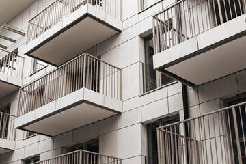 Modern apartment building facade with stacked balconies. Repetitive metal railings and geometric lines on residential block exterior. Urban housing architecture detail in city district.