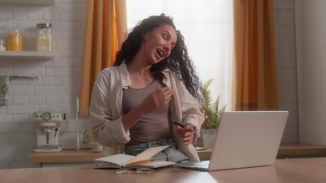 Happy Latina business woman talking mobile phone typing laptop write notes home smiling Hispanic female businesswoman girl using computer smartphone multitask freelance homeowner remote work kitchen