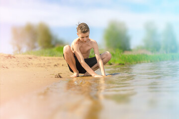 Fototapeta premium Boy Playing with Sand at Lakeside on a Sunny Day