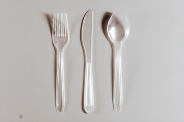 Clear plastic fork, knife, and spoon arranged in a row on a neutral surface with no food present during the daytime