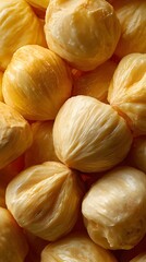 Close-up of several peeled fruit segments with a glossy, smooth texture and golden-yellow hue, showcasing their natural layers and fibrous details, filling the entire frame
