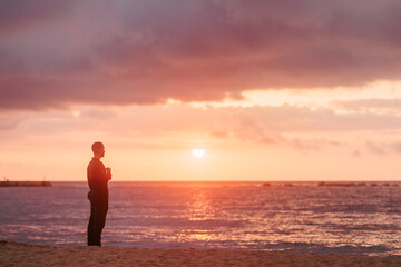 Fototapeta premium Young man meditating on beach at colorful sunset