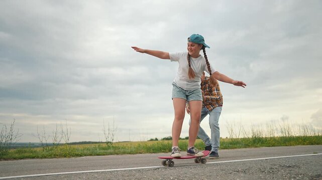 A child stands on skateboard with arms extended, learning to balance. Father helps child keep balance outdoors. Fun activity, skateboarding, and family play together. Kid learning new skills.