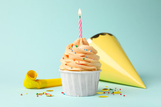 Yummy cupcake with sprinkles, burning candle and party items on light blue background