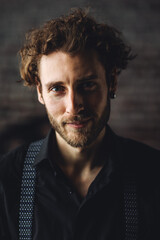 Obraz premium Young sexy handsome fit elegant man in a black shirt looking at camera posing for a photoshoot in a studio. Loft interior, stylish outfit, men's wear, casual clothing. Idea for grooms style, posing