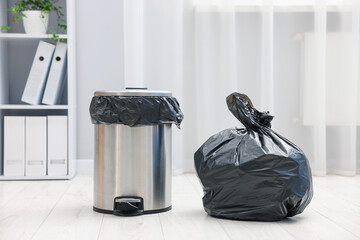 Metal trash bin and plastic bag with garbage on floor indoors