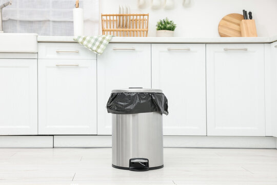 Metal trash bin with plastic bag on floor in kitchen