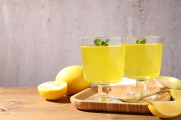 Fototapeta premium Yummy yellow jelly in dessert bowls, mint and fresh lemons on wooden table, closeup. Space for text