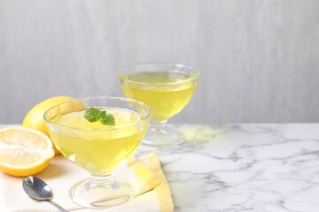 Fototapeta premium Yummy yellow jelly in dessert bowls, mint and fresh lemons on white marble table, closeup. Space for text