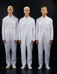 three blond people wearing white coveralls on a black background