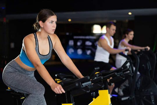 Determined young girl training with spin bike in fitness hall during full-body workout