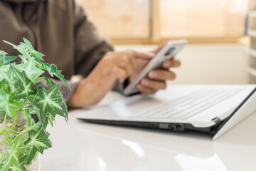 窓際の明るい室内でテレワークをする男性のイメージ（手前の植物にピント、顔無し）_スマホ 