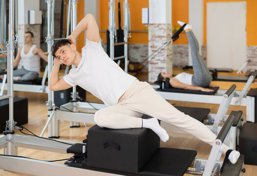 Man with help of informer is engaged in Pilates studio and performs exercises to strengthen muscles of press. Round-robin training for athletes during preparation for competitions