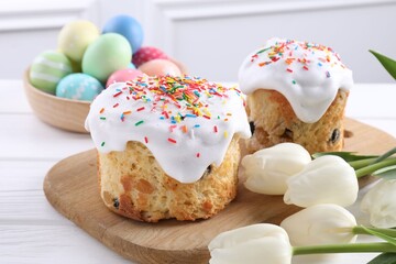 Delicious Easter cakes, painted eggs and tulips on white wooden table, closeup