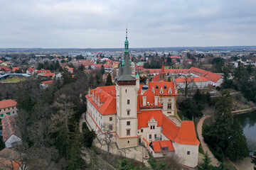 Obraz premium Aerial view of Průhonice Castle near Prague, Czech Republic, featuring red rooftops, historic architecture, surrounding parkland, and a cloudy autumn sky. default