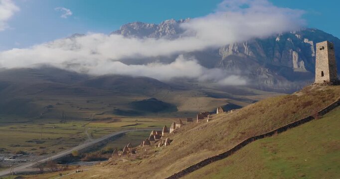 Aerial View of Dargavs City of the Dead in North Ossetia Russia with Ancient Stone Crypts and Watchtower Against High Mountains and Clouds, Camera Zoom In.