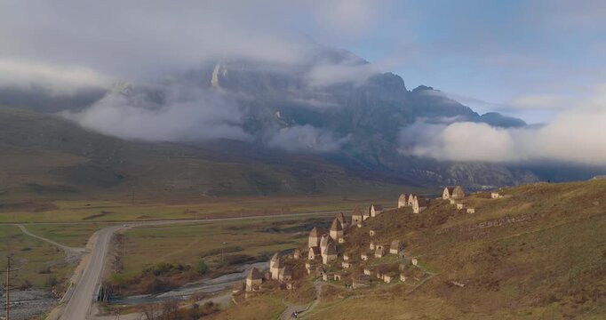 The camera rises towards the historical ruins of the Dargavs "City of the Dead" necropolis, revealing the mysterious site against misty Caucasus Mountains.