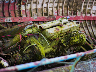 A green engine is sitting on a pile of debris in an old wooden fishing boat. The engine is rusted and old, and it is in a state of disrepair. The scene is bleak and desolate.