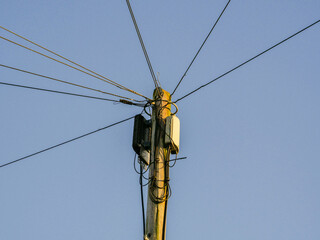 A tall pole with wires coming out of it. The sky is blue and clear. The pole is surrounded by wires and is the center of attention. Superfast cable internet connection. Technology.