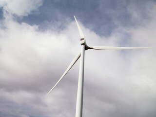 A wind turbine is standing in a field with a cloudy sky in the background. Scene is calm and peaceful, as the wind turbine is a symbol of renewable energy and the natural beauty of the landscape