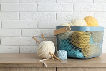 Knitting yarns and needles on wooden table near white brick wall. Space for text