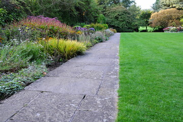 Obraz premium Stone paved path in a beautiful garden with a grass lawn and colourful flowers