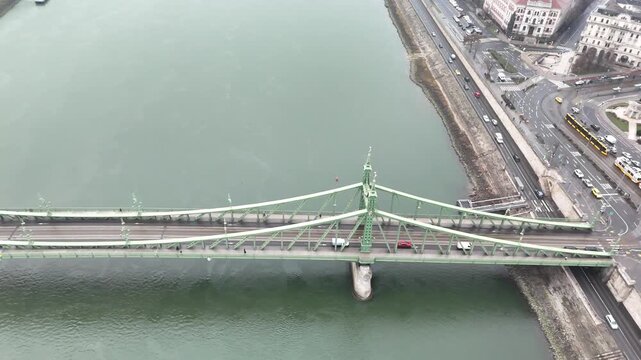 Aerial pans left from a top-down perspective, revealing the full green ironwork of the Liberty Bridge (Szabads&aacute;g h&iacute;d) spanning the Danube River in Budapest, Hungary