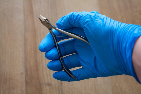Hand in glove holding professional manicure and pedicure tool, stainless steel cuticle clipper, cuticle cutter