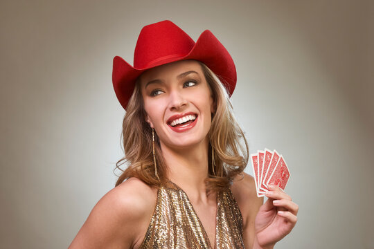 Woman wearing red cowboy hat and gold sequin top holds playing cards while smiling