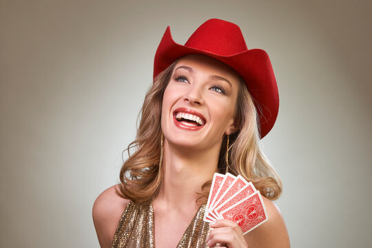 Woman wearing red cowboy hat smiling while holding playing cards in gold sequined top