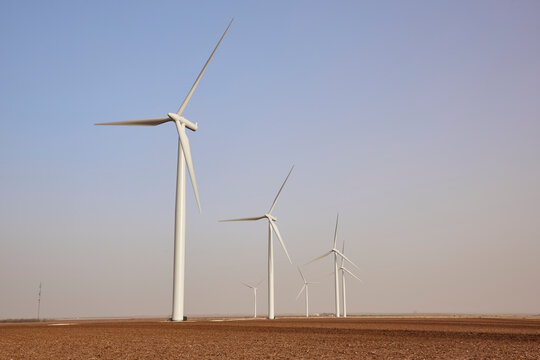 White wind turbines generating renewable energy across an open agricultural field under clear skies