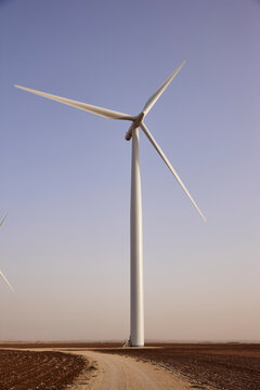 White wind turbine with three blades stands tall against a clear sky in rural farmland
