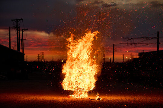 Large bonfire burns brightly on urban street at dusk with dramatic orange flames and embers