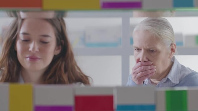 Female Pharmacist Recommending Cough Syrup to Senior Woman at Pharmacy Shelves