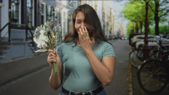 Woman holding a bouquet and covering her mouth with her hand on a street with bicycles and row houses; surprise gratitude.