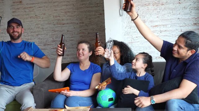 Friends clinking beer bottles and toasting while watching football soccer at home, celebrating the match together. Sports camaraderie, adult friendship, social drinking, relaxed home atmosphere