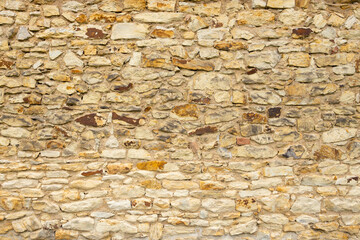 Textured stone wall featuring a variety of beige and brown stones with visible mortar joints, creating a rustic and natural appearance suitable for architectural design
