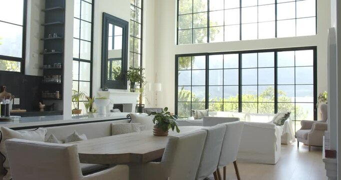 Camera panning and tilting right, revealing wood dining table, bench and tall windows filling room