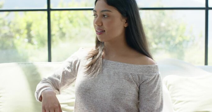 African American woman in top spreading arms laughing on couch by multi-pane window as sun drawing