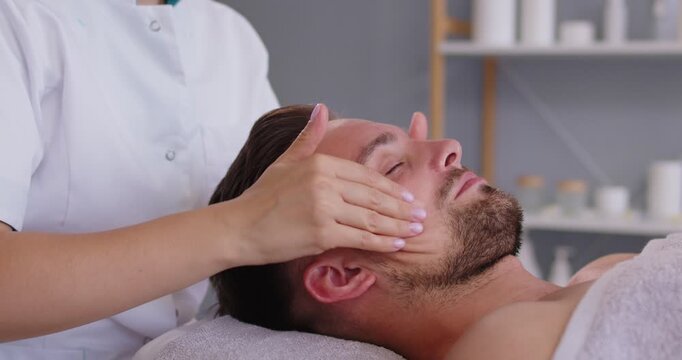 Relaxed man client receives a facial massage from cosmetologist in spa salon clinic. Beauty procedure for skin treatment in beauty clinic from beautician to male person. Wellness concept. 