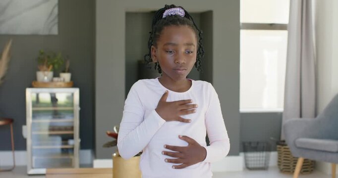 African child placing hands on chest and abdomen, practicing breathing to calm in living room