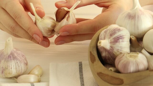 Woman peeling fresh garlic at white wooden table, closeup