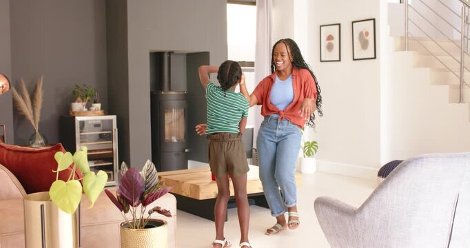 African American mother stepping, child reaching up and twirling greeting in living room by stove