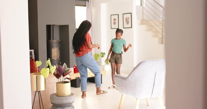 African American mother dancing with teenage daughter, encouraging mirroring sandal tap at home